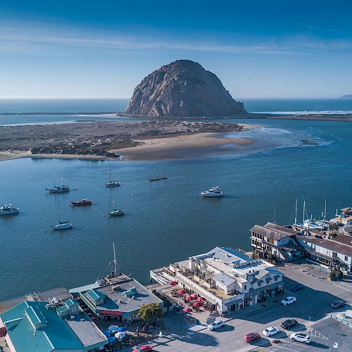 This image shows a coastal town with boats docked in a marina, a large rock formation in the background, and buildings near the waterfront ending the sentence.