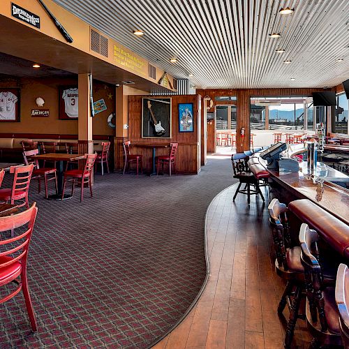 This image shows a sports-themed bar and restaurant with red chairs, sports memorabilia on the walls, and a view of a marina through the windows.