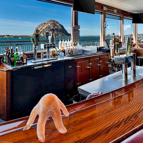 A bar with a view of a large rock in the ocean, featuring various drinks and a starfish on the counter.