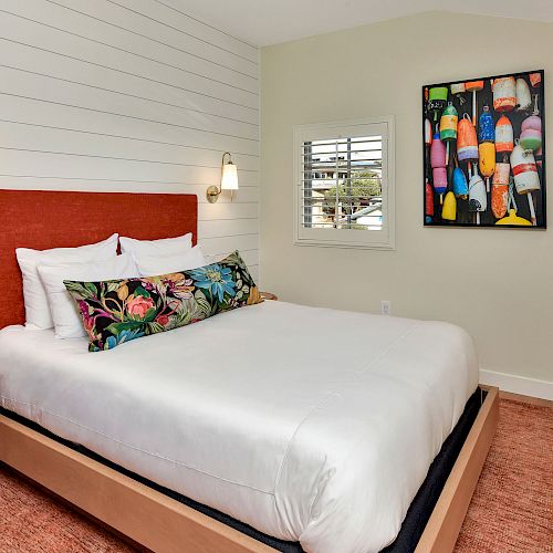 A cozy bedroom with a white bed, colorful pillows, wall-mounted lamps, vibrant art, and a side table on a textured rug, having a serene ambiance.