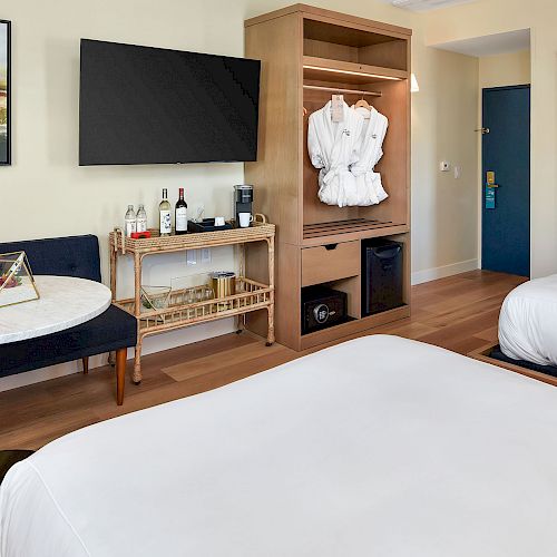 This image shows a hotel room with two beds, a small round table, a TV, and an open closet with robes.