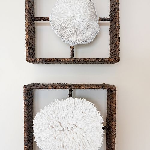 Two wooden square frames each containing a white, textured, spherical object, mounted on a light-colored wall.