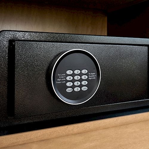 The image shows a black electronic safe placed inside a wooden shelf, with a keypad for entering a security code to unlock it.