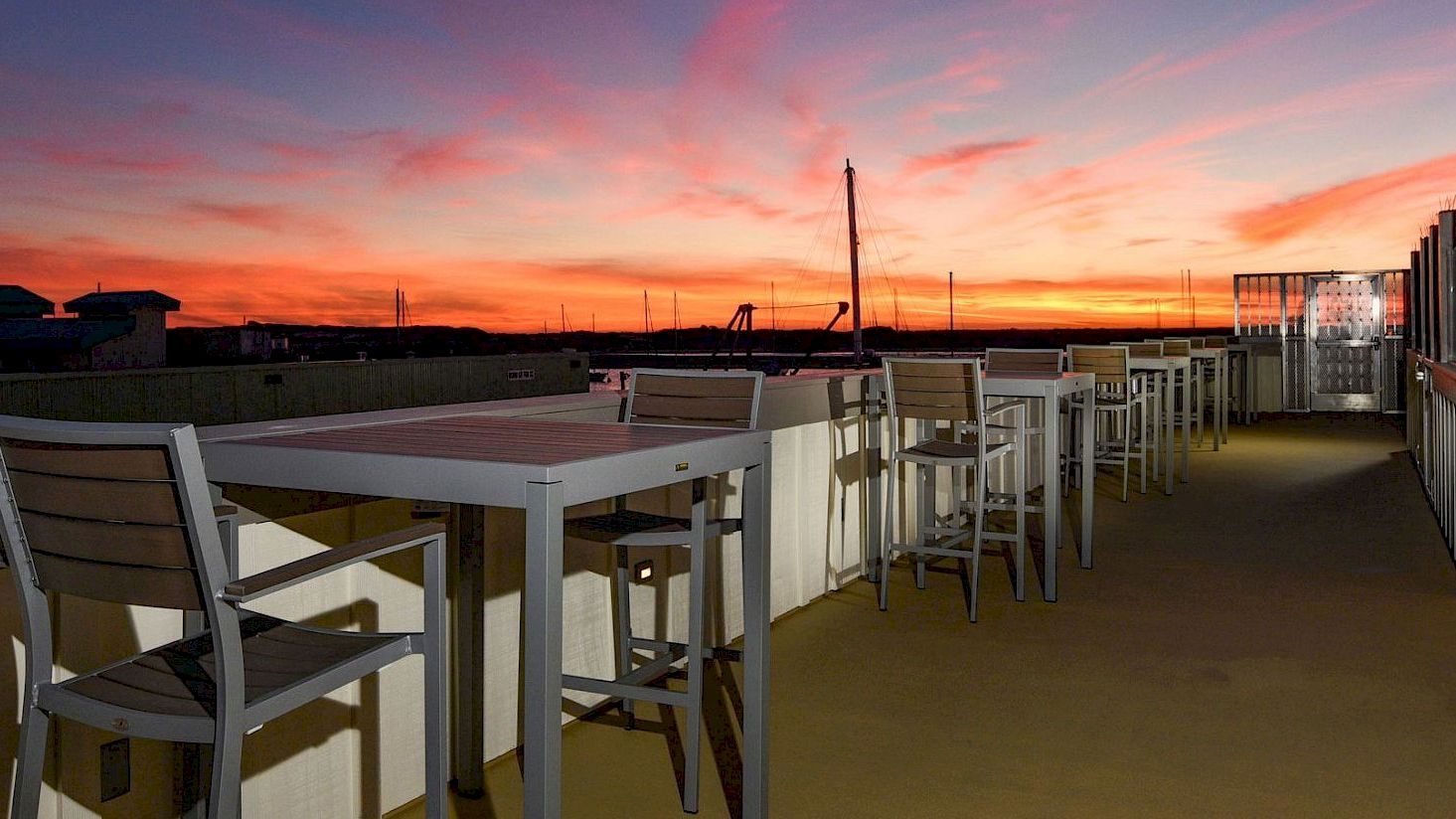 Rooftop patio with tables and chairs, overlooking a vibrant sunset sky, creating a peaceful and inviting atmosphere.