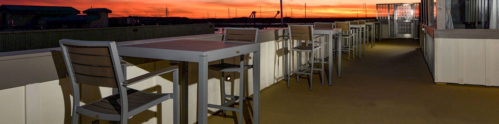 Rooftop patio with tables and chairs, overlooking a vibrant sunset sky, creating a peaceful and inviting atmosphere.