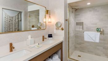 A modern bathroom featuring a vanity with a sink, mirror, towels, and a spacious shower area, with elegant lighting and amenities.