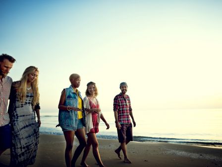 A group of five people walking along the beach at sunset, enjoying each other's company and the serene view of the ocean.